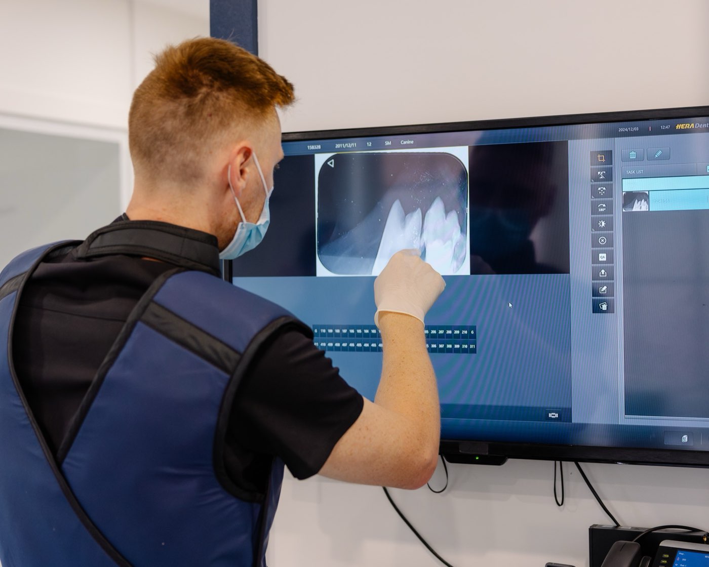A team member in a lead apron reviewing a dental X-ray of a dog's tooth roots on a screen